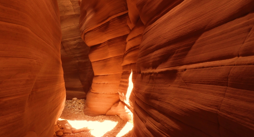 The sun shines through into a red slot canyon